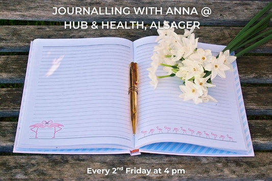 Open notebook with a pen and flowers on a wooden surface, promoting a journalling event at Hub & Health