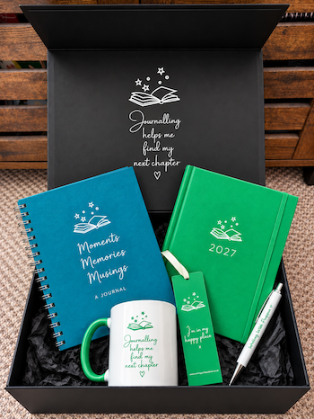 A curated journaling gift set presented in an open black box, including a teal spiral journal, a green 2027 diary, a white mug, a green bookmark, and a white pen, all with journalling-themed graphics and text.
