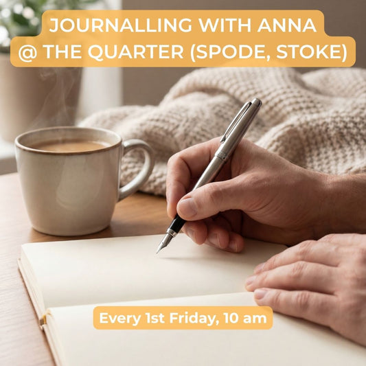 A person writing in an open notebook with a silver pen, with a mug of coffee and a knitted blanket in the background. Orange text overlays read 'JOURNALLING WITH ANNA @ THE QUARTER (SPODE, STOKE)' and 'Every 1st Friday, 10 am'.